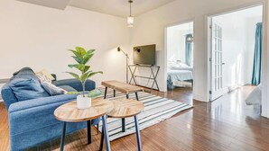 A modern living room with a sofa, a coffee table, a potted plant, and a TV. - St. Laurent Apt with Balcony & Skylight Near Parks (Montréal)