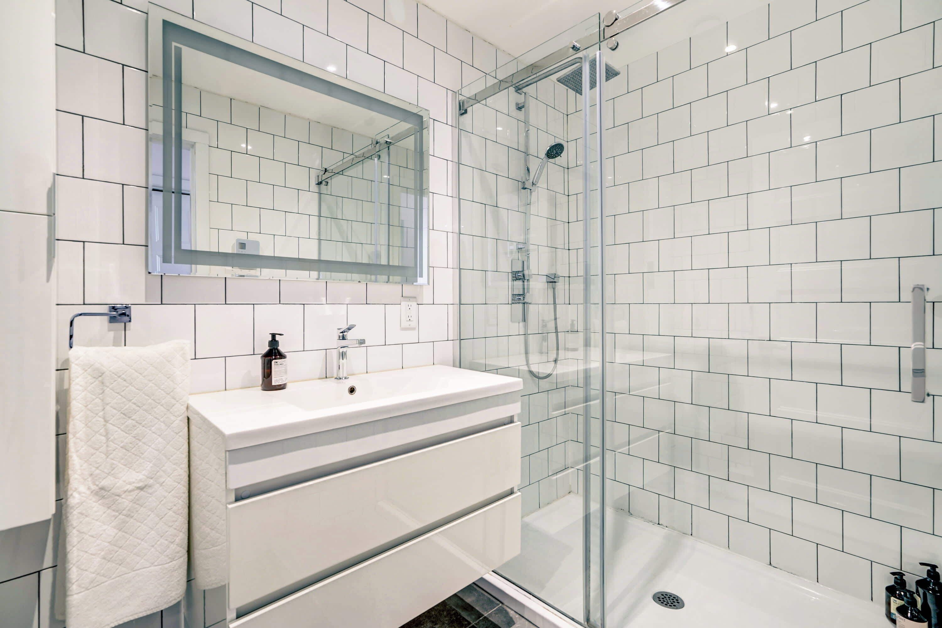 A modern bathroom with a glass-enclosed shower, a white vanity with a mirror, and a tiled floor.