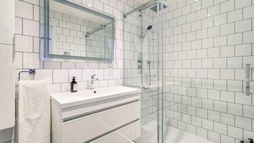 A modern bathroom with a glass-enclosed shower, a white vanity with a mirror, and a tiled floor.