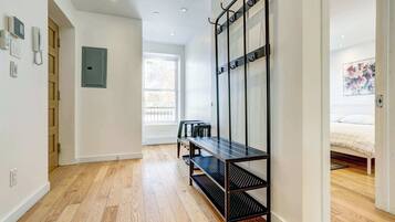 Une chambre moderne avec un plancher en bois, une étagère en métal noir, une porte verte et un lit recouvert d’une couvre-lit à motifs floraux.