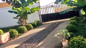 Una entrada con reja y un camino de concreto, rodeada de follaje y plantas en macetas.