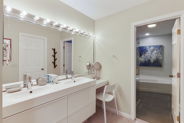 A bathroom with a large vanity, a mirror with lights, a chair, and a bathtub.