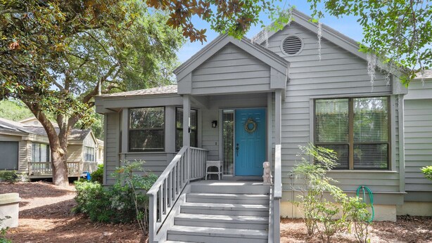 Une maison de plain-pied avec un porche à l’avant, une porte bleue et un petit jardin devant.