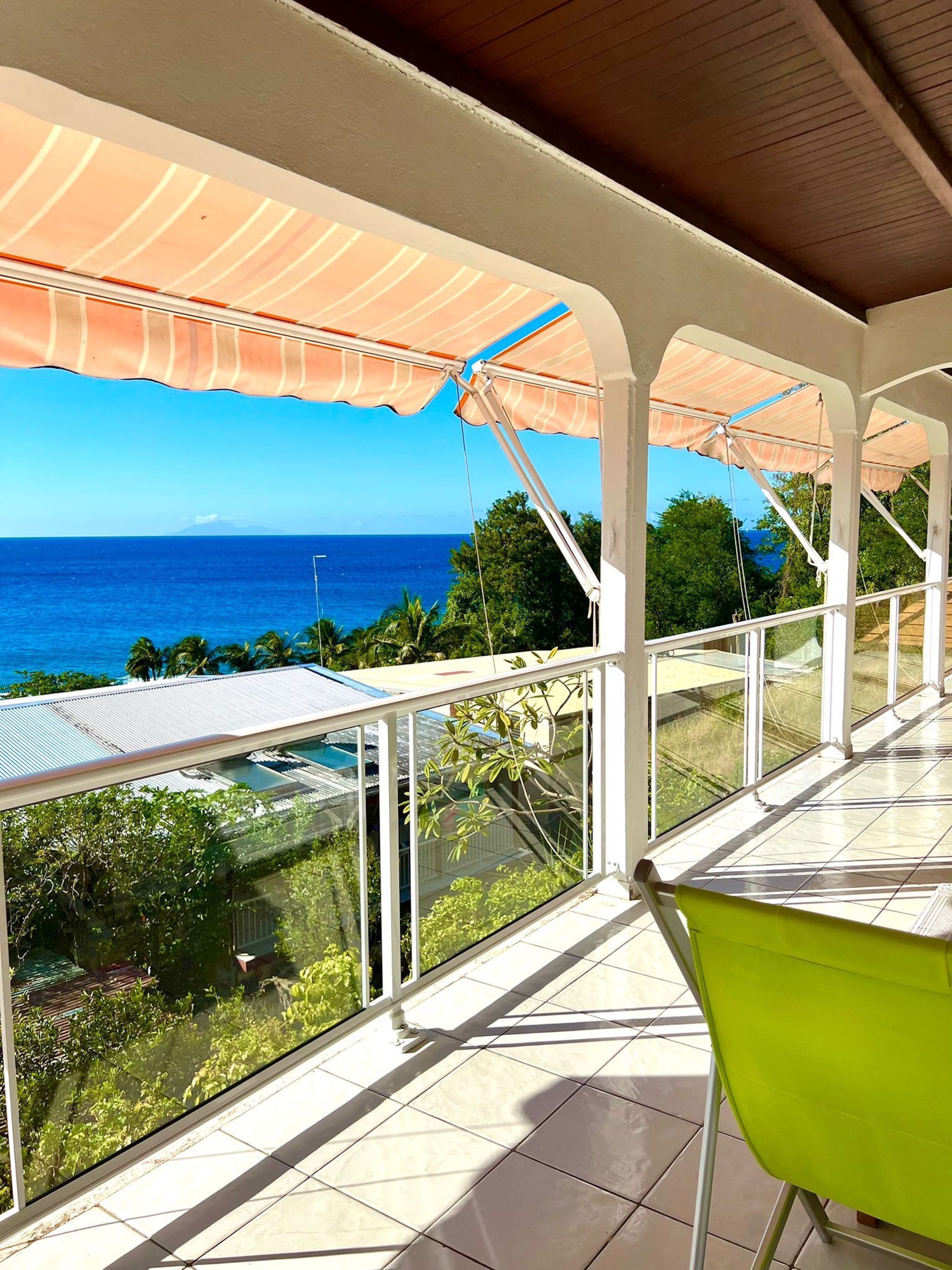 A covered balcony with a view of the ocean, a green chair, and a tiled floor.