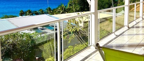 A covered balcony with a view of the ocean, a green chair, and a tiled floor.