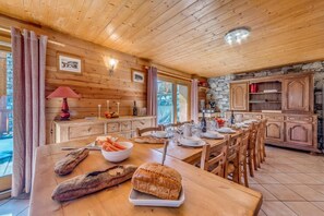 A wooden cabin interior with a dining table set for a meal, a stone fireplace, and wooden cabinets.