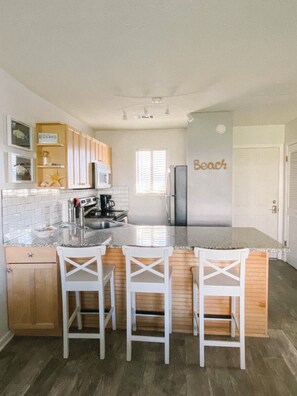 A kitchen with a central island, three white bar stools, a refrigerator, and a microwave. - Affordable 30A Getaway! Updated studio condo close to the beach! Near Seaside. (Santa Rosa Beach,)