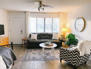Relax in this inviting living room with a sofa, coffee table, and armchair, perfect for unwinding with a good book or watching TV.