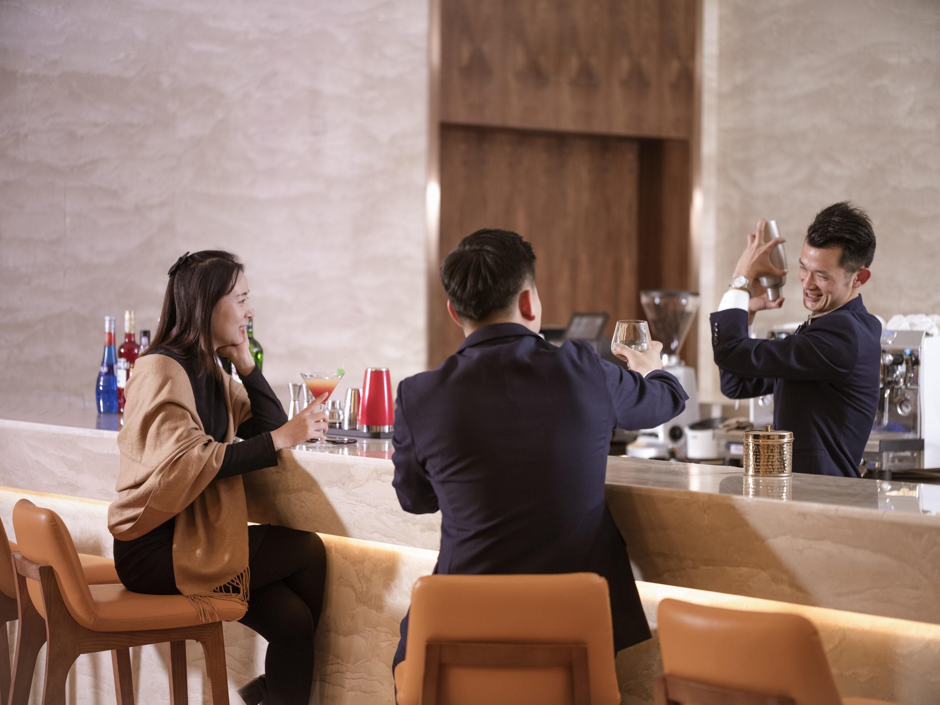 A bar area with a counter, bar stools, and a person preparing a drink.