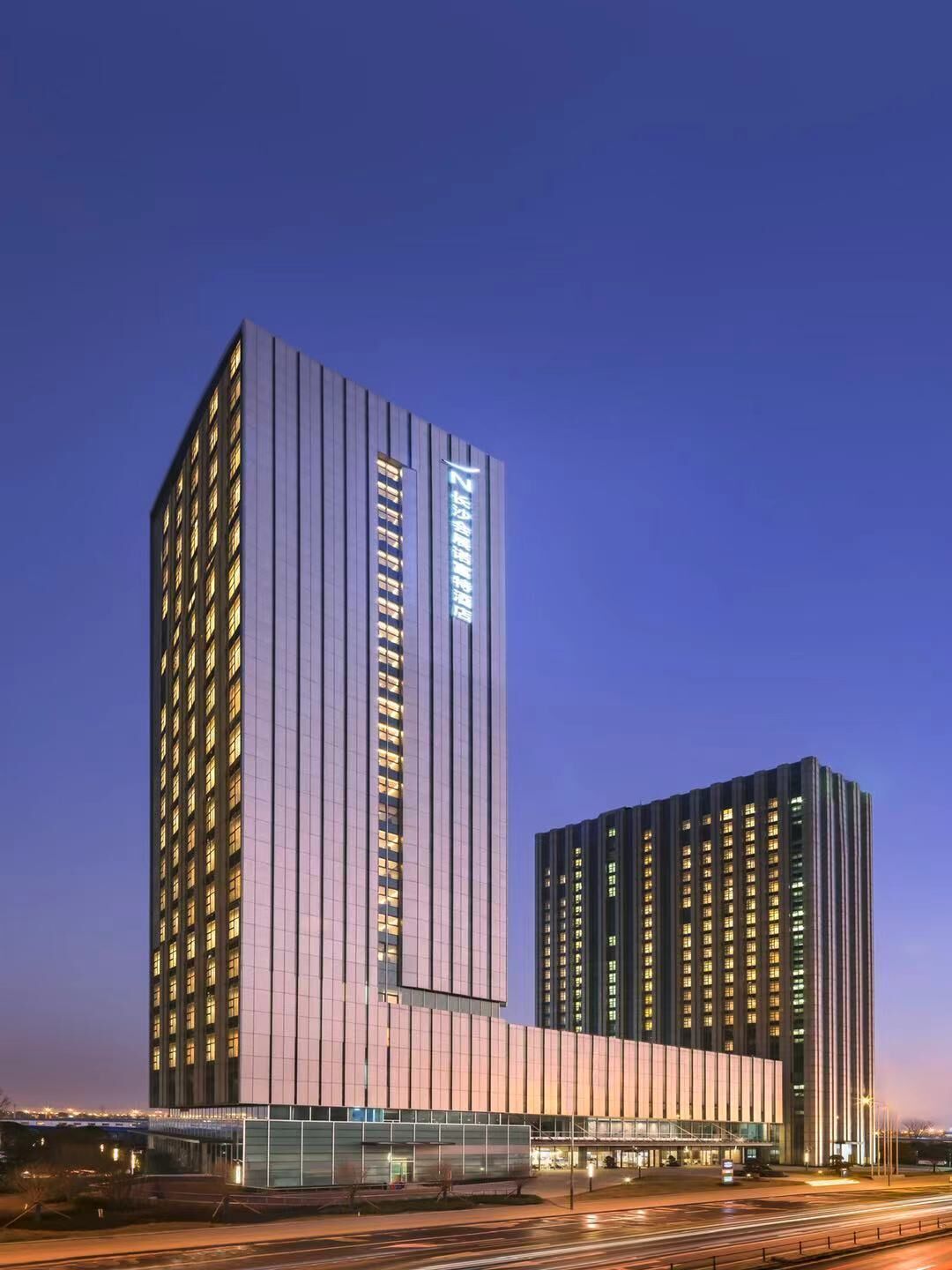A modern hotel with a tall, rectangular building featuring a prominent vertical light strip and a shorter building with a similar design.