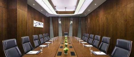 A conference room with a long wooden table, black leather chairs, and recessed lighting.