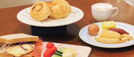 A breakfast setting with croissants, a sandwich, eggs, tomatoes, cucumbers, and a cup of coffee on a table.