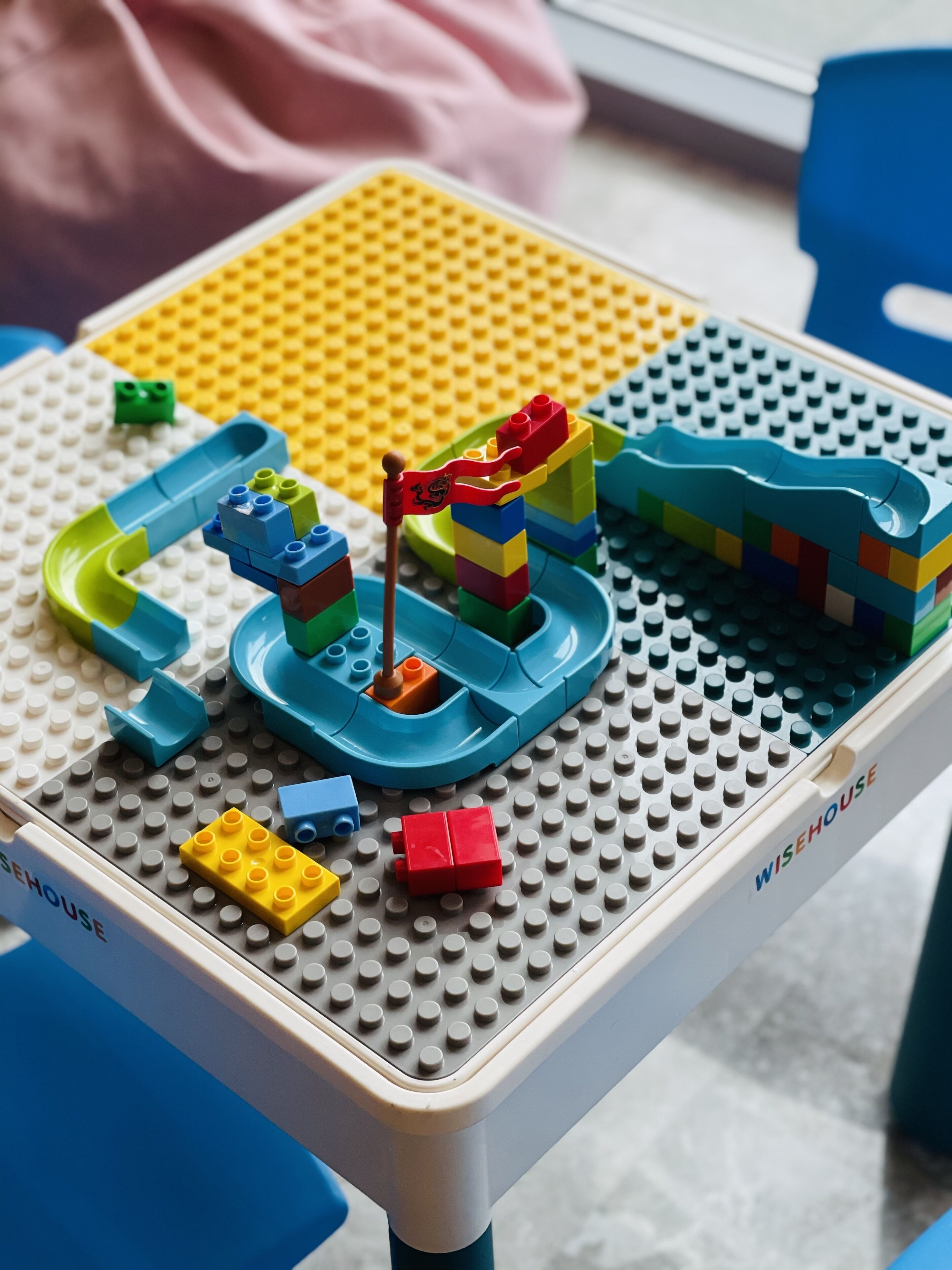 LEGO-leikkisetti on pöydällä, ja siinä on merkintä ”WISEHOUSE”. Setissä on liukumäki, vesiliukumäki ja erilaisia värikkäitä palikoita.