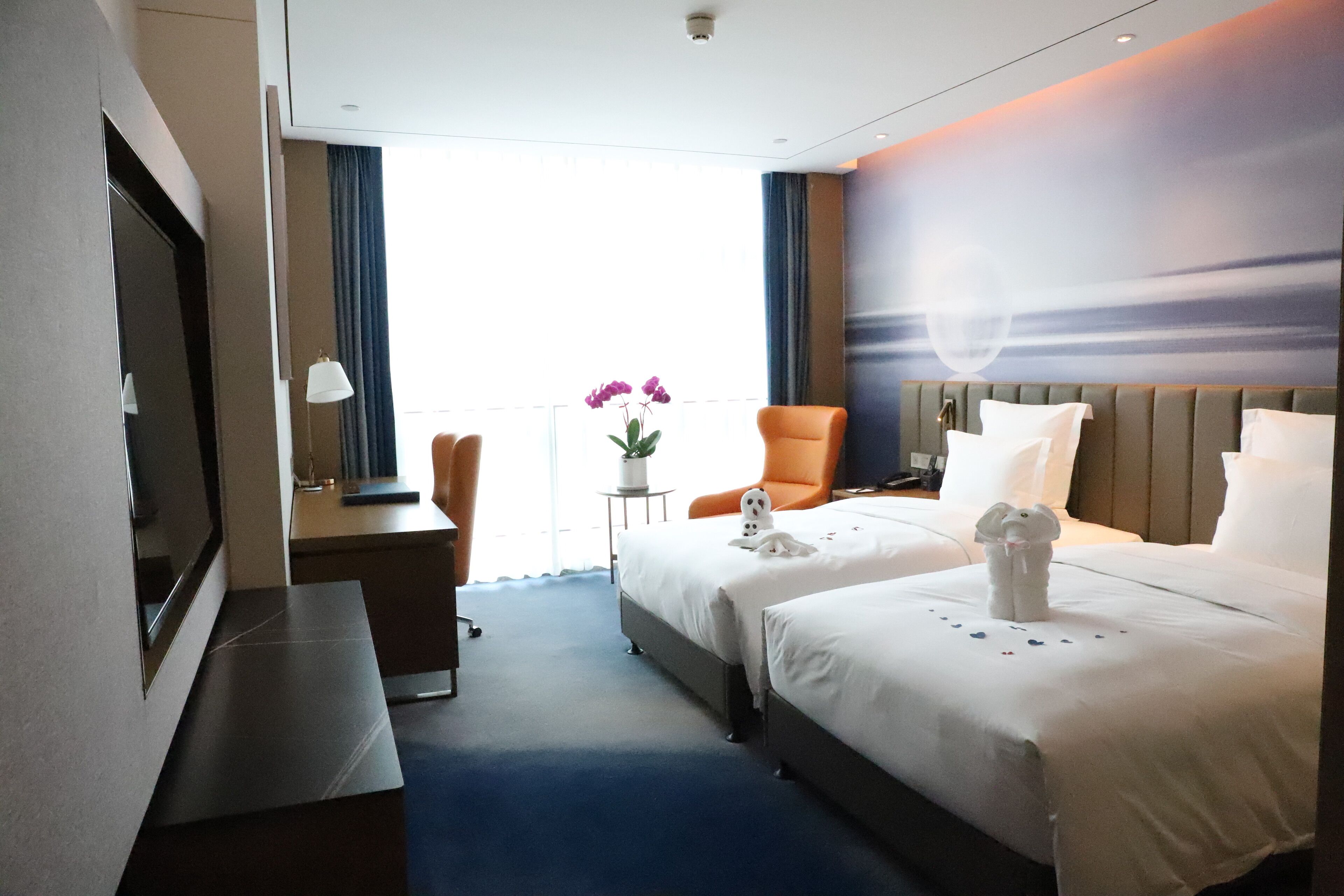 Habitación de hotel con dos camas, un escritorio, una silla, un televisor y vistas al exterior.