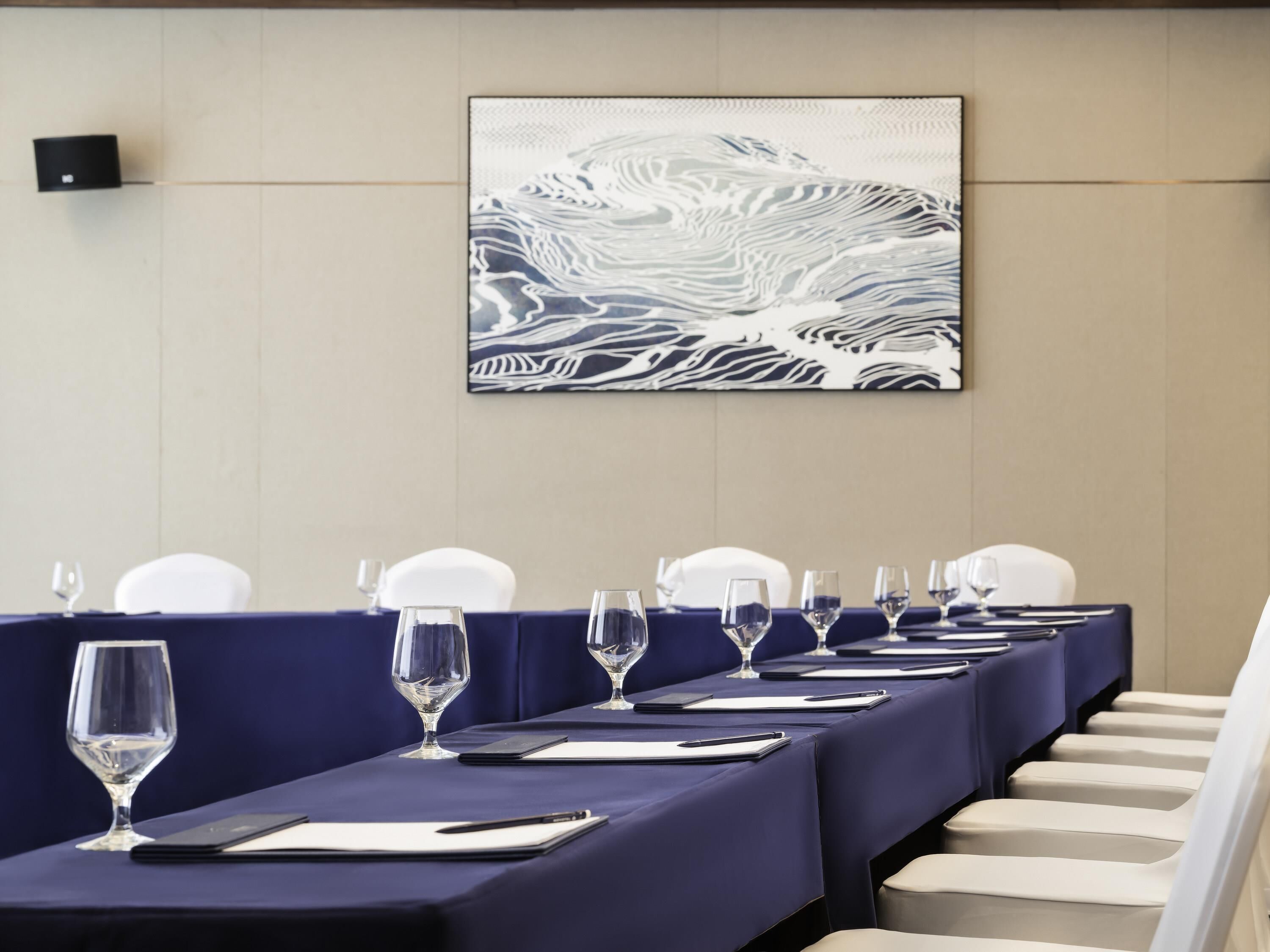 A conference room with a long table set for a meeting, white chairs, and a large abstract painting on the wall.