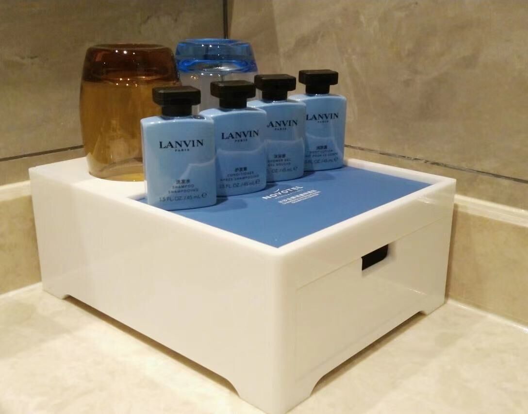 Una encimera de baño con una bandeja blanca que contiene varias botellas de champú Lanvin y un frasco azul de aceite para el cabello.