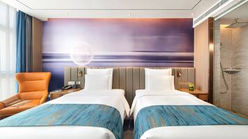 A hotel room with two beds, a large window with curtains, a wall-mounted TV, and a shower area.