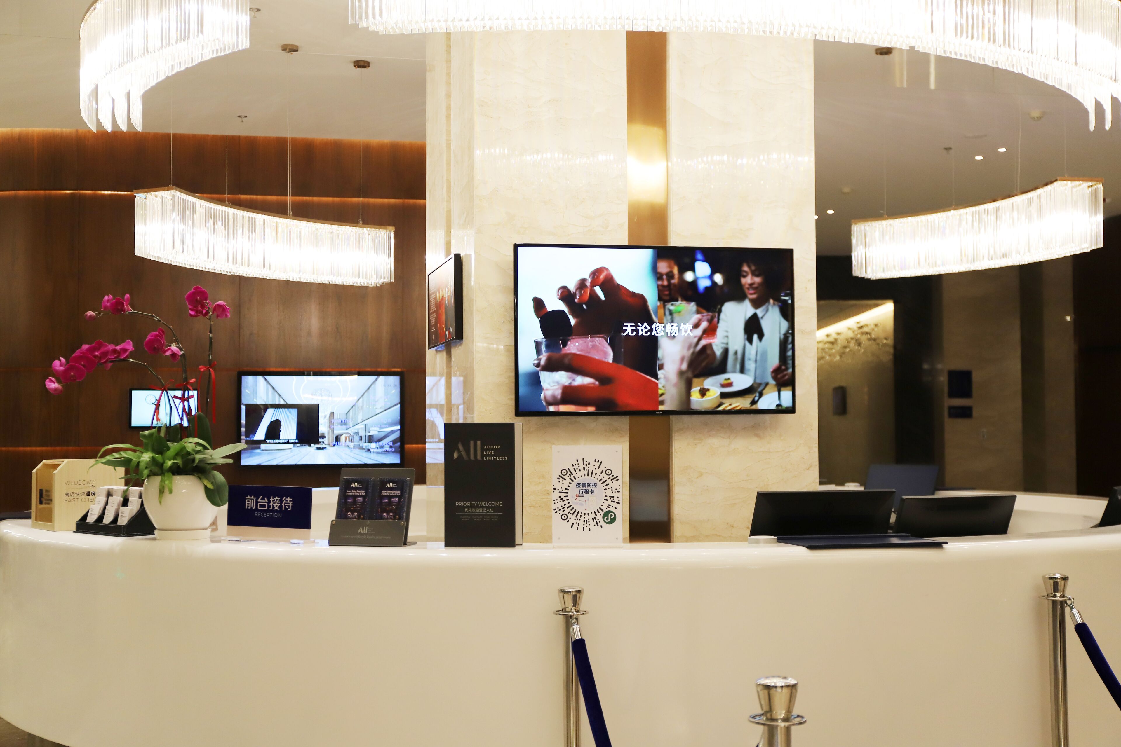 A hotel reception desk with a TV screen, a potted plant, and a sign.