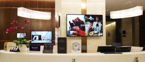 A hotel reception desk with a TV screen, a potted plant, and a sign.