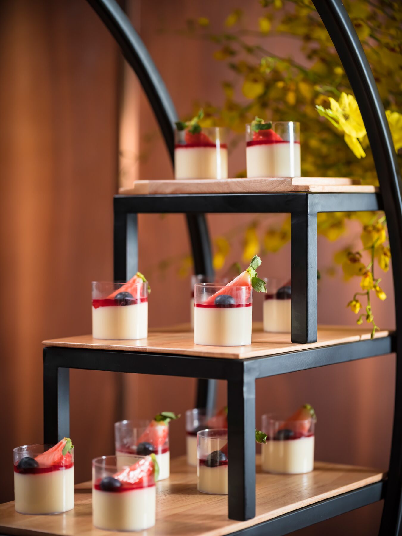 Een presentatie van desserts op een etagère van hout, met meerdere glazen bekers gevuld met gelaagde desserts en verse fruitdecoraties.