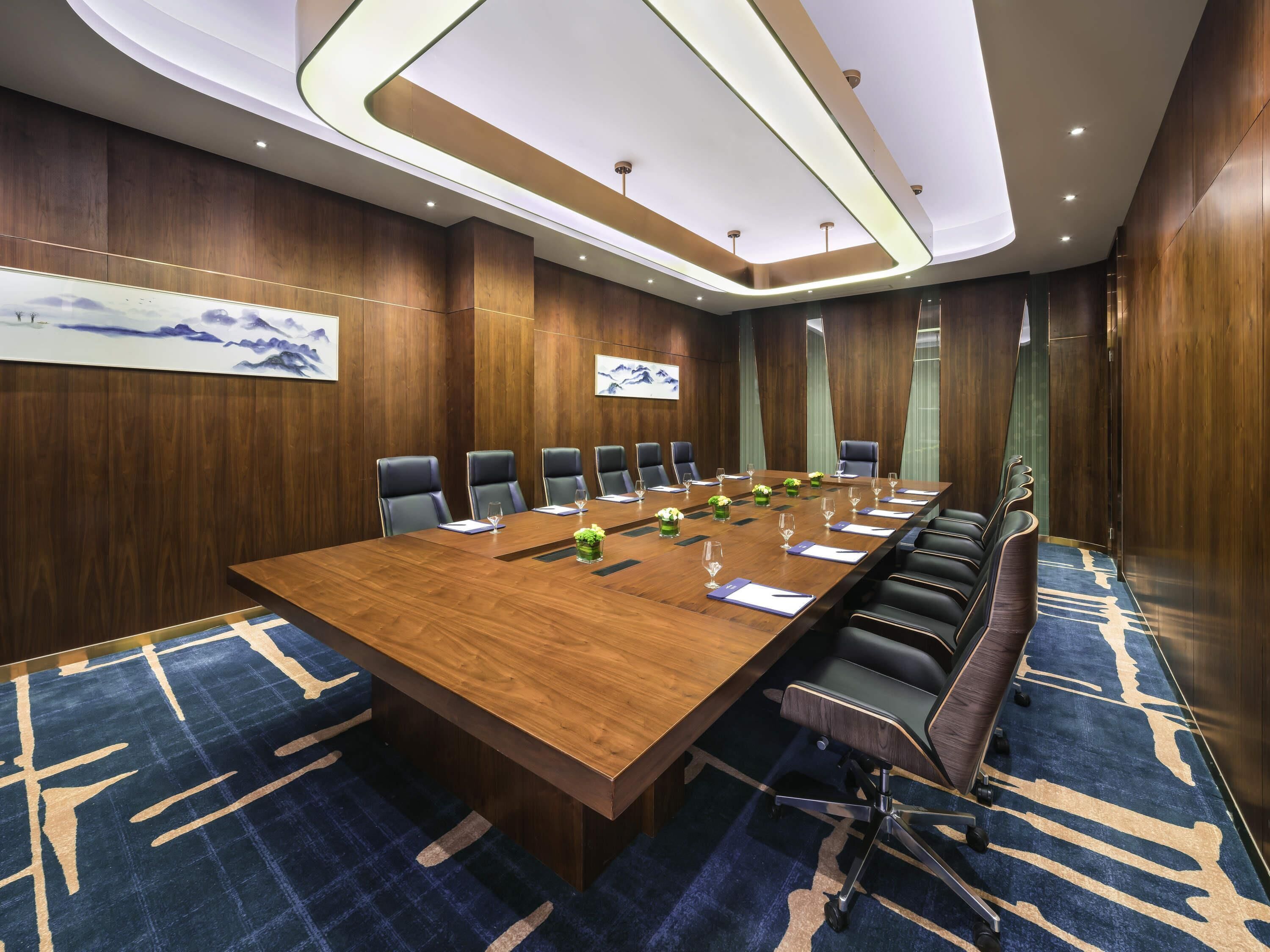 A conference room with a long wooden table, black chairs, and a blue carpet.