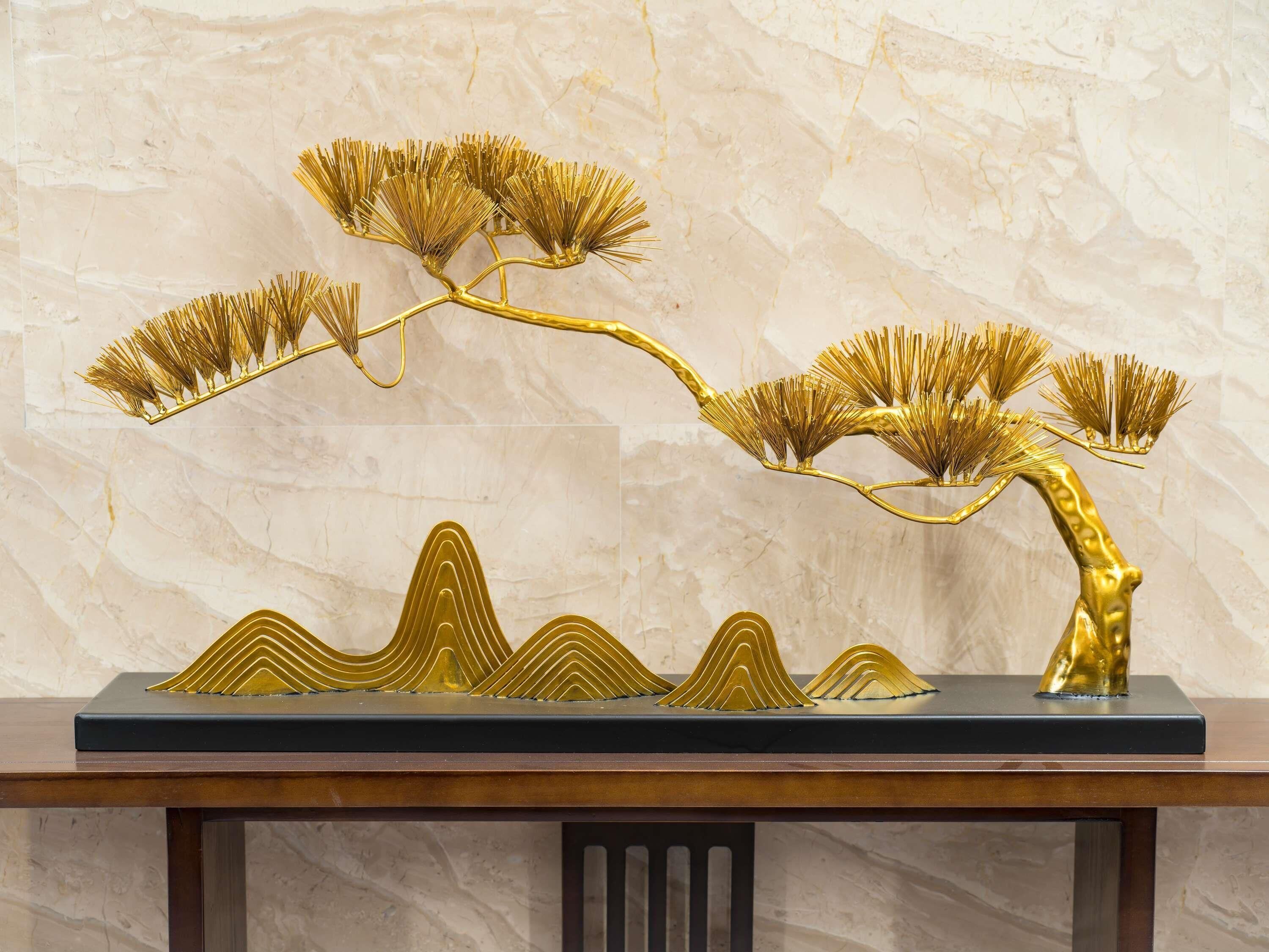 A golden tree sculpture on a black base, set against a marble wall.