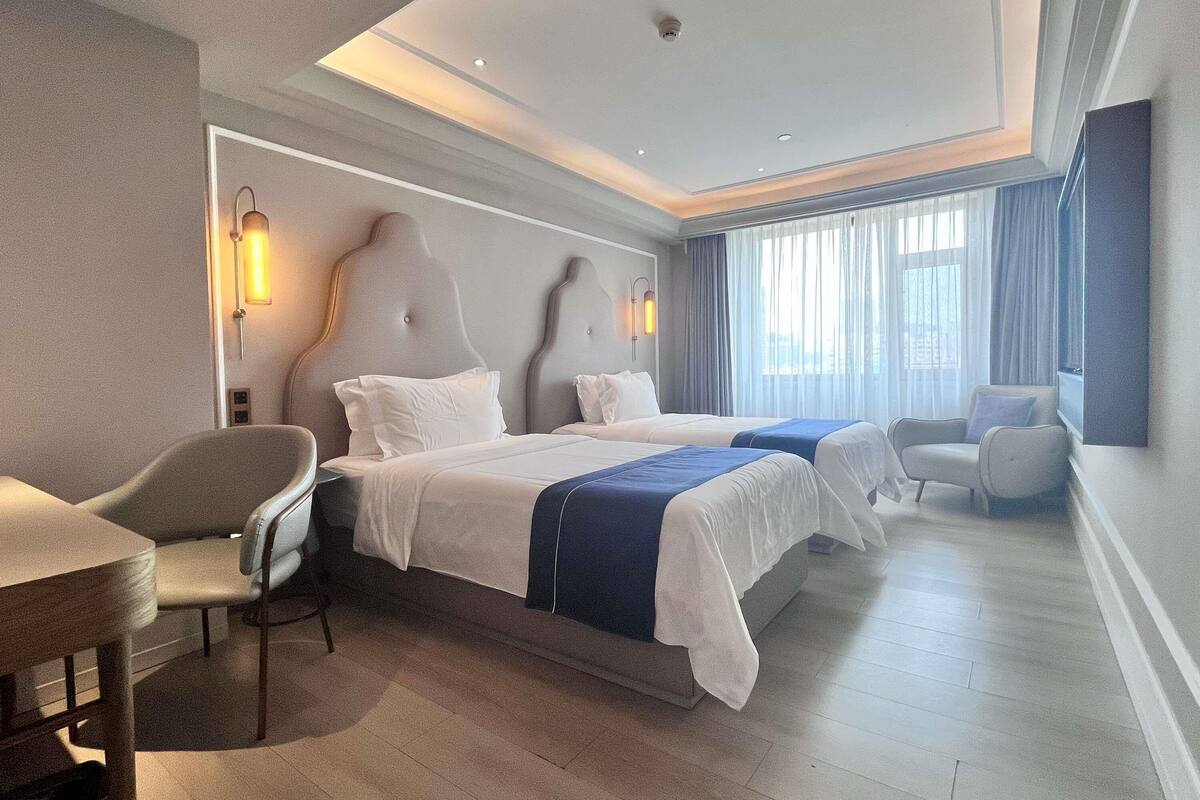 A hotel room with a large bed, two bedside tables, a chair, a desk, and a window with curtains.