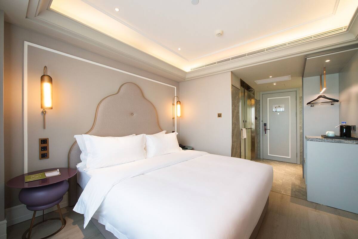 A hotel room with a large bed, bedside lamps, a small table, and a door leading to a bathroom.