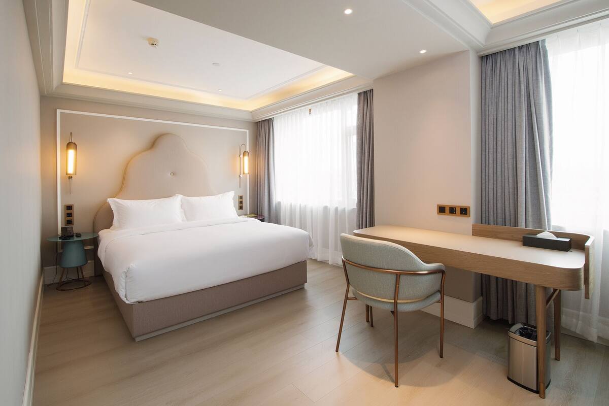 A hotel room with a bed, a desk, a chair, and a trash bin.