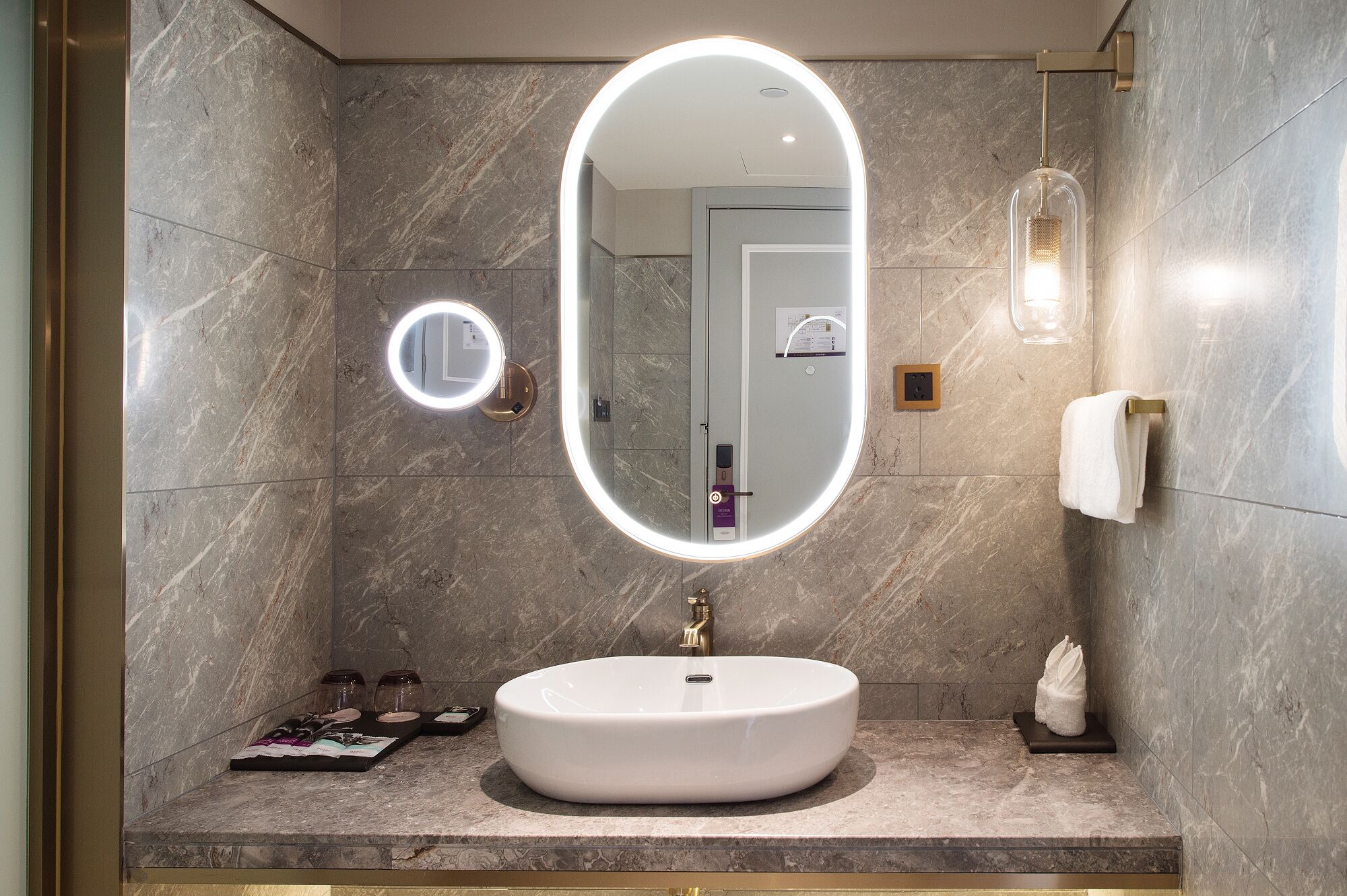 Une salle de bain avec un miroir rond, un lavabo et un porte-serviettes.