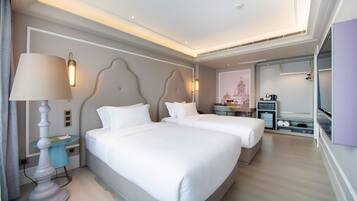 A hotel room with two beds, a desk, a lamp, and a kitchenette.