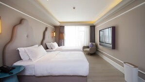 Habitación de hotel con dos camas, un escritorio con teléfono, una silla, un televisor y un cubo de basura.