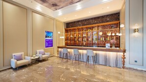 Un hall de entrada con mostrador de recepción de mármol, taburetes de bar, zona de estar con sofás y una pantalla digital en la pared.