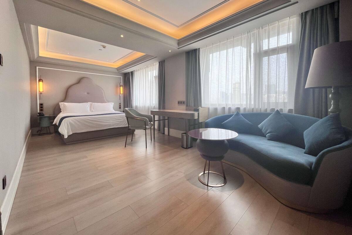 A modern hotel room with a bed, a sofa, a small table, and a chair.