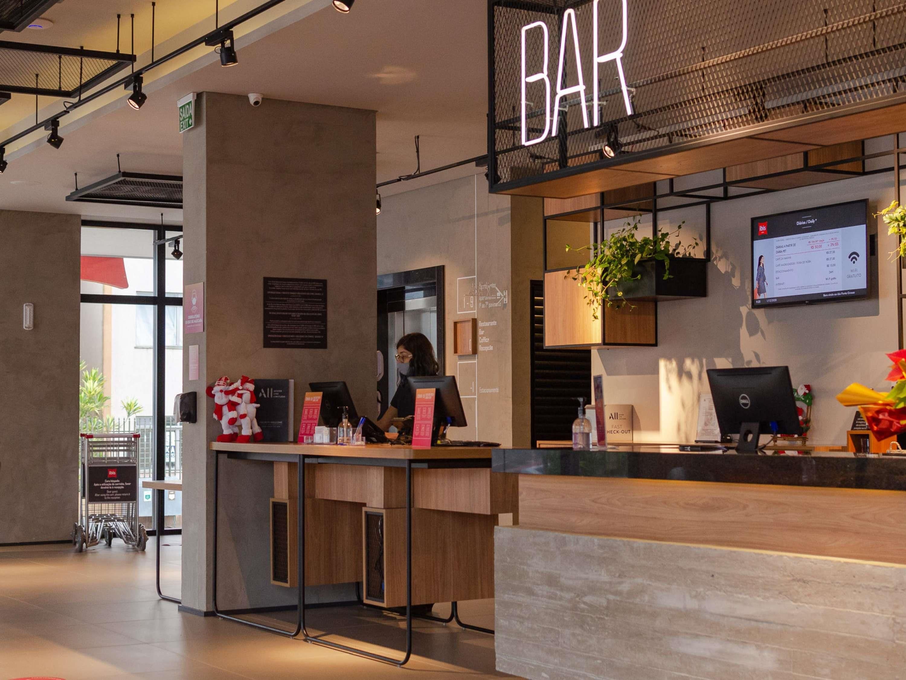 A modern bar area with a digital menu display, a reception desk, and a seating area with a plant.