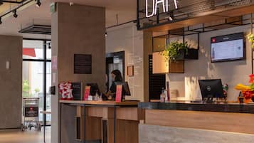 A modern bar area with a digital menu display, a reception desk, and a seating area with a plant.