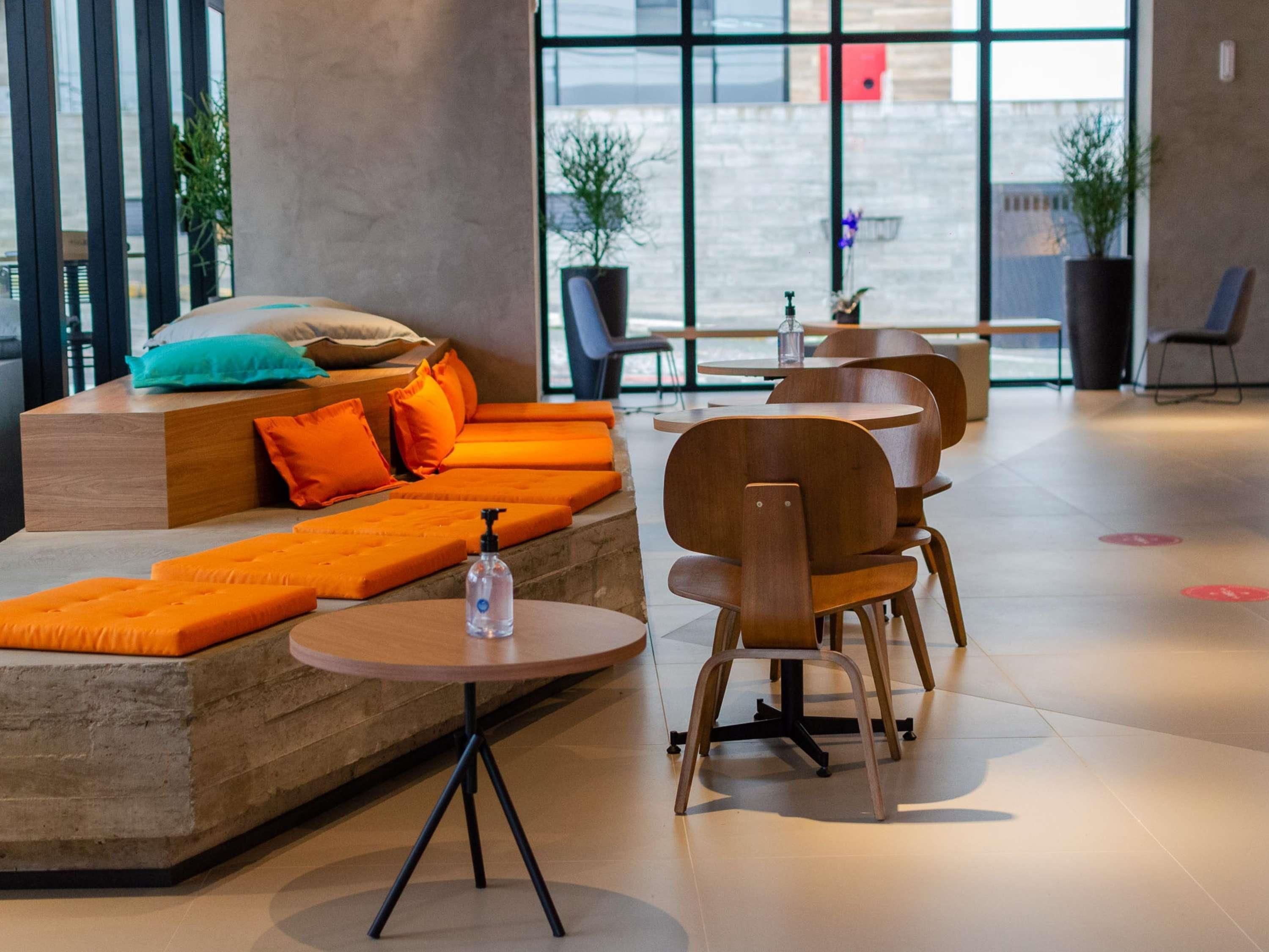 Un área de estar moderna con sofá y sillones, una mesita con una botella, y amplias ventanas.