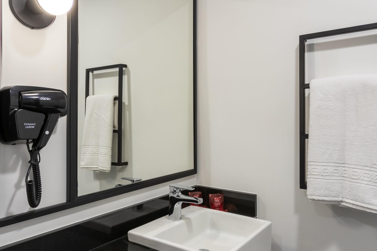 A bathroom with a large mirror, a hair dryer, a sink, and a towel rack.