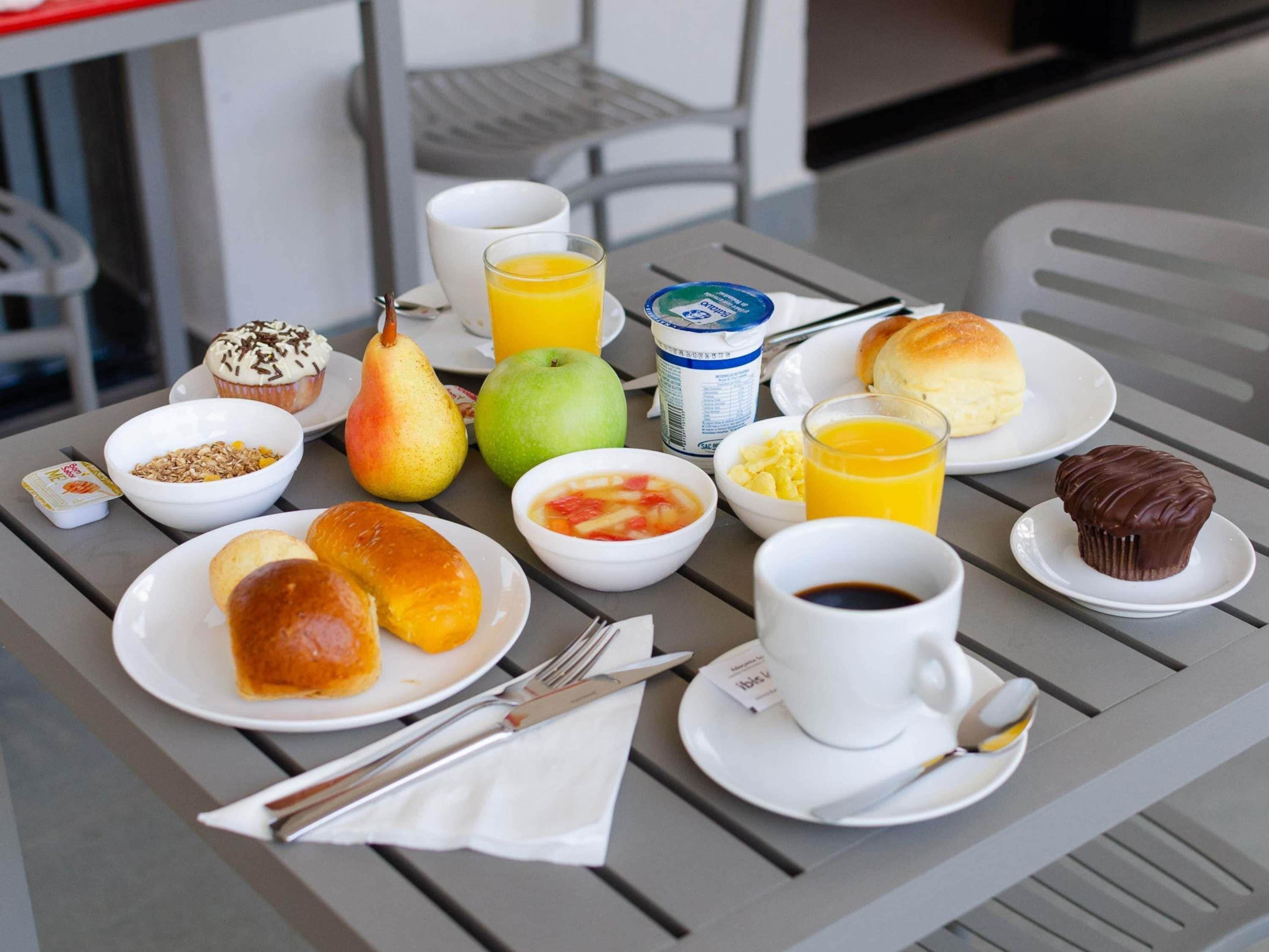 Una mesa de desayuno con diferentes alimentos, como frutas, pasteles y bebidas.