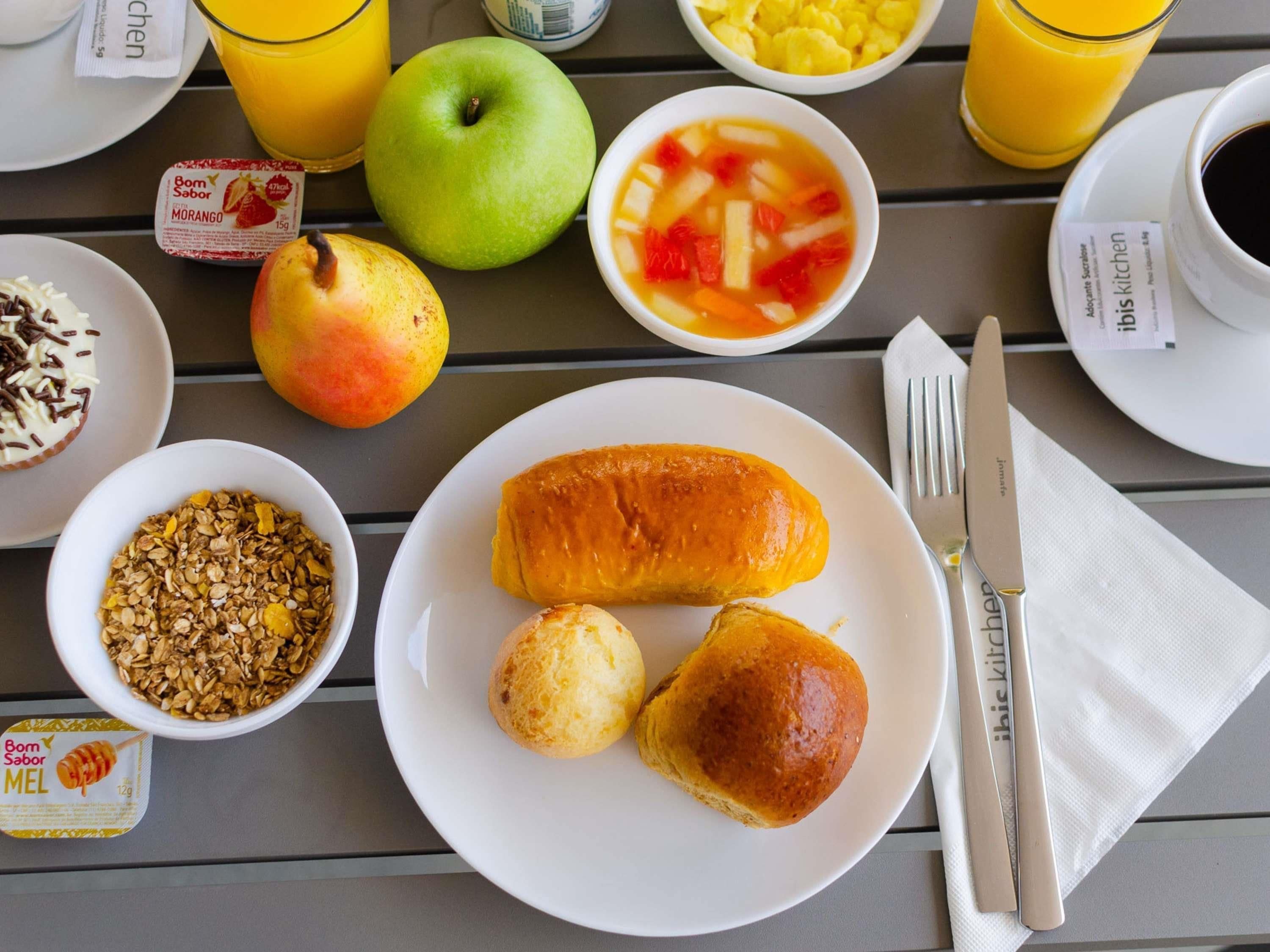 A breakfast setting with a plate of pastries, a bowl of fruit, and a glass of orange juice.