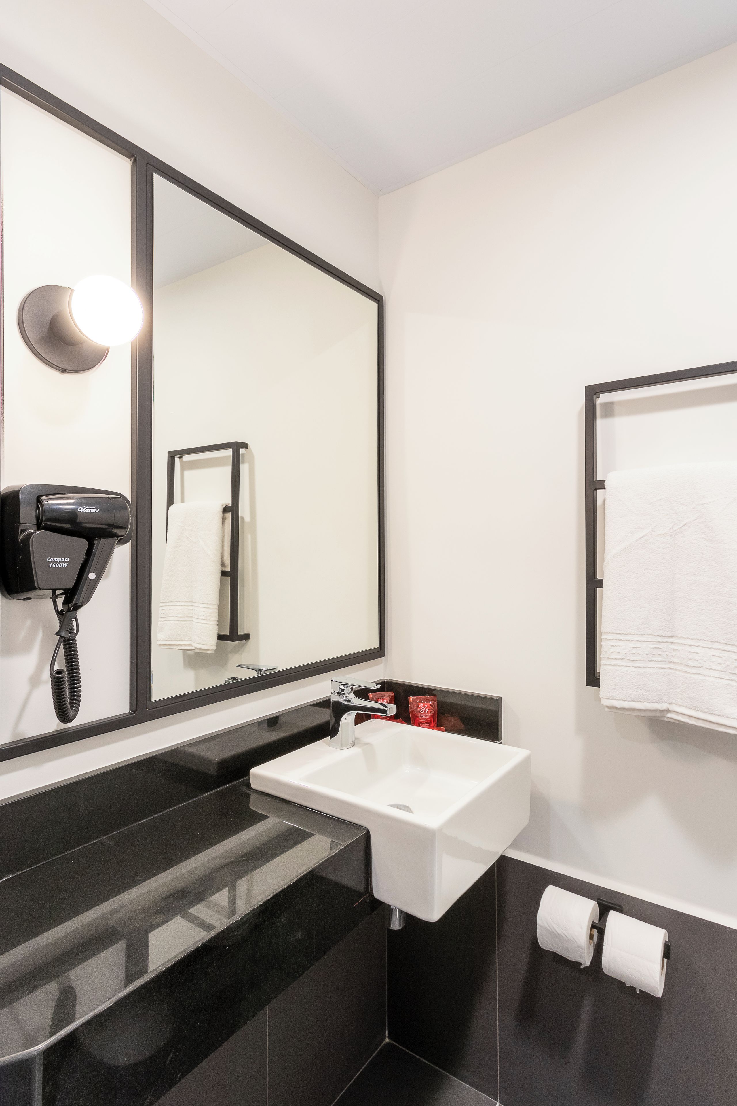 A modern bathroom with a large mirror, a hairdryer, a sink, and a towel rack.