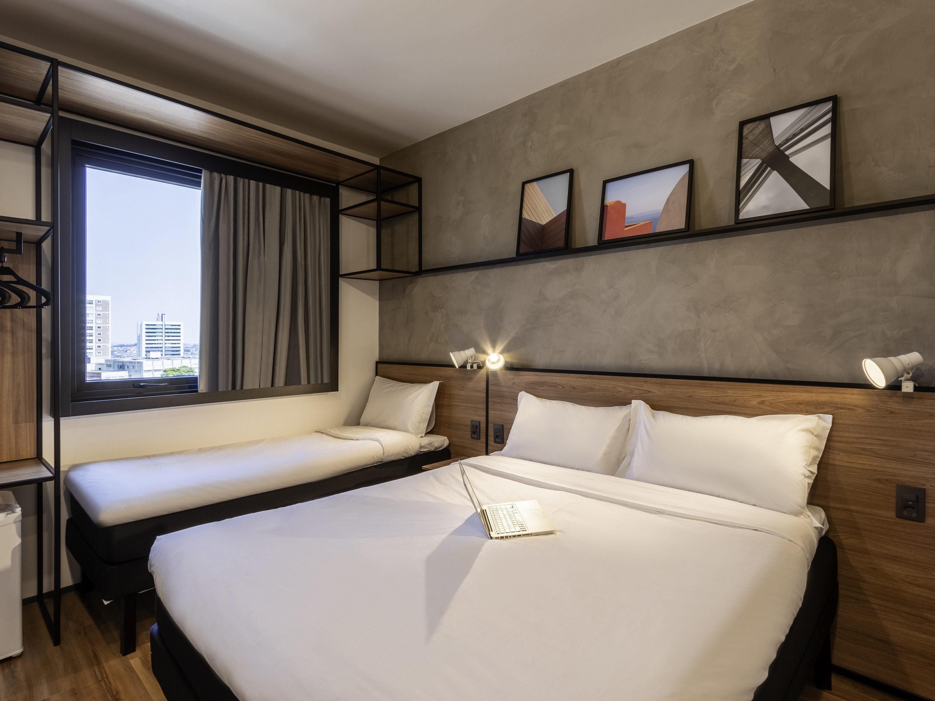 Une chambre d’hôtel moderne avec un grand lit, un lit plus petit, un bureau et une fenêtre donnant sur la ville.