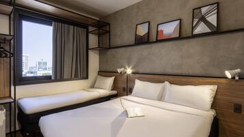 Una habitación de hotel moderna con una cama grande, una cama más pequeña, un escritorio y una ventana con vistas a la ciudad.