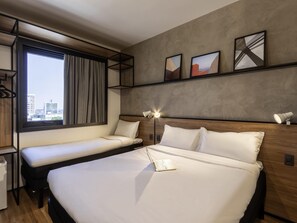 Una habitación de hotel moderna con una cama grande, una cama más pequeña, un escritorio y una ventana con vistas a la ciudad.