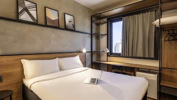 Una habitación de hotel moderna con una cama grande, un escritorio con una computadora portátil, un armario y una ventana con cortinas.