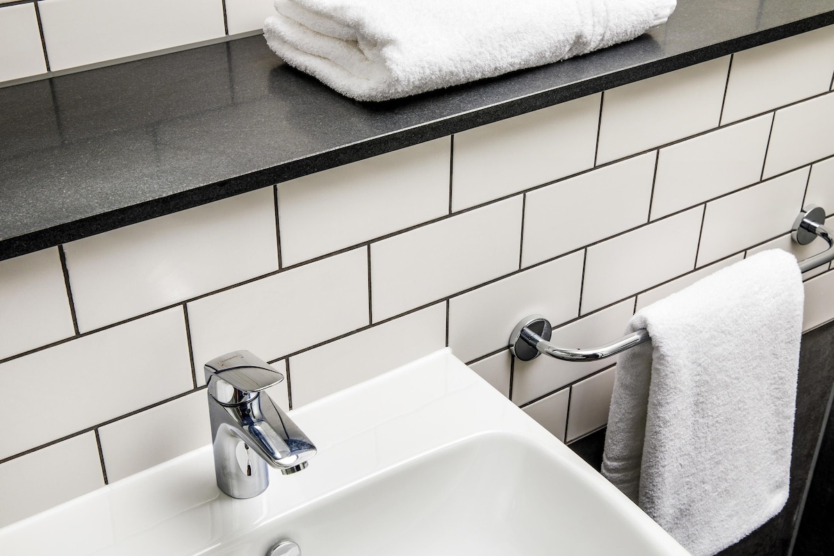 Ein Badezimmer mit einem weißen Waschbecken, einer schwarzen Arbeitsplatte und weißen Fliesenwänden.