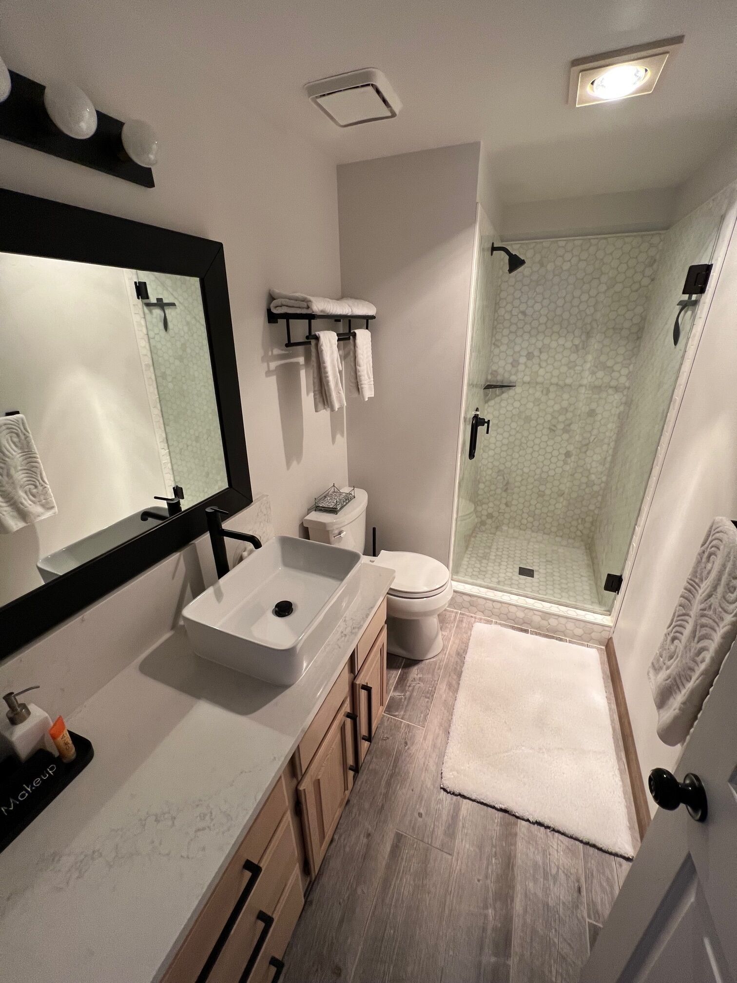 A modern bathroom with a large mirror, a white sink, a toilet, and a glass-enclosed shower.