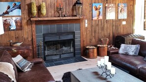 Ein gemütliches Blockhaus-Interieur mit Kamin, Holzwänden, einem Ledersofa und einem Couchtisch.