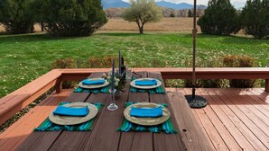 Eine Holzdielen-Terrasse mit Tisch für vier Personen, blauem Geschirr und Servietten, sowie einem großen Sonnenschirm, der Schatten spendet.