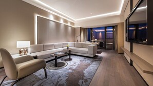 Et moderne hotelværelse med en hjørnesofa, et sofabord, et fjernsyn og et stort vindue med udsigt.